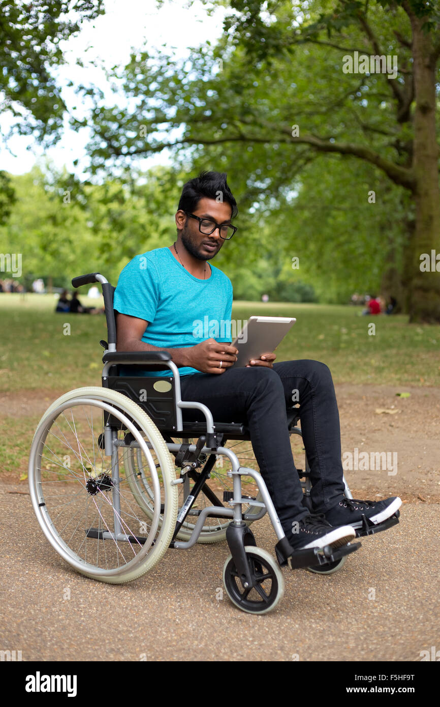 junger Mann in einem Rollstuhl mit einem Tabletcomputer Stockfoto