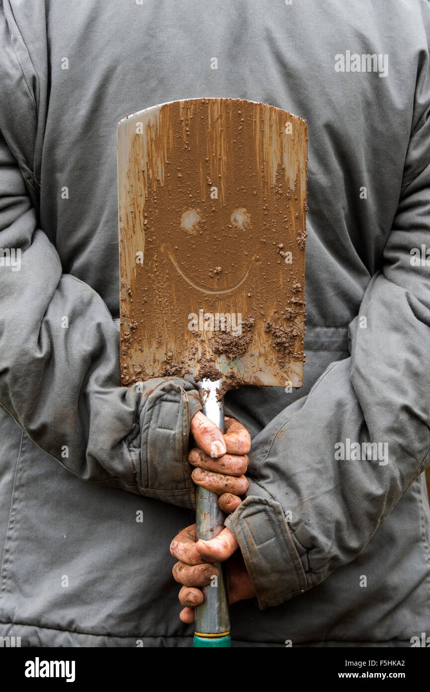 Gärtner hält einen Smiley schlammigen Spaten Stockfoto