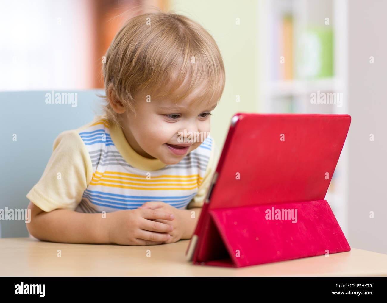 Nettes Kind Kleinkind Jungen mit Tablet-pc sitzt am Tisch im Haus Stockfoto