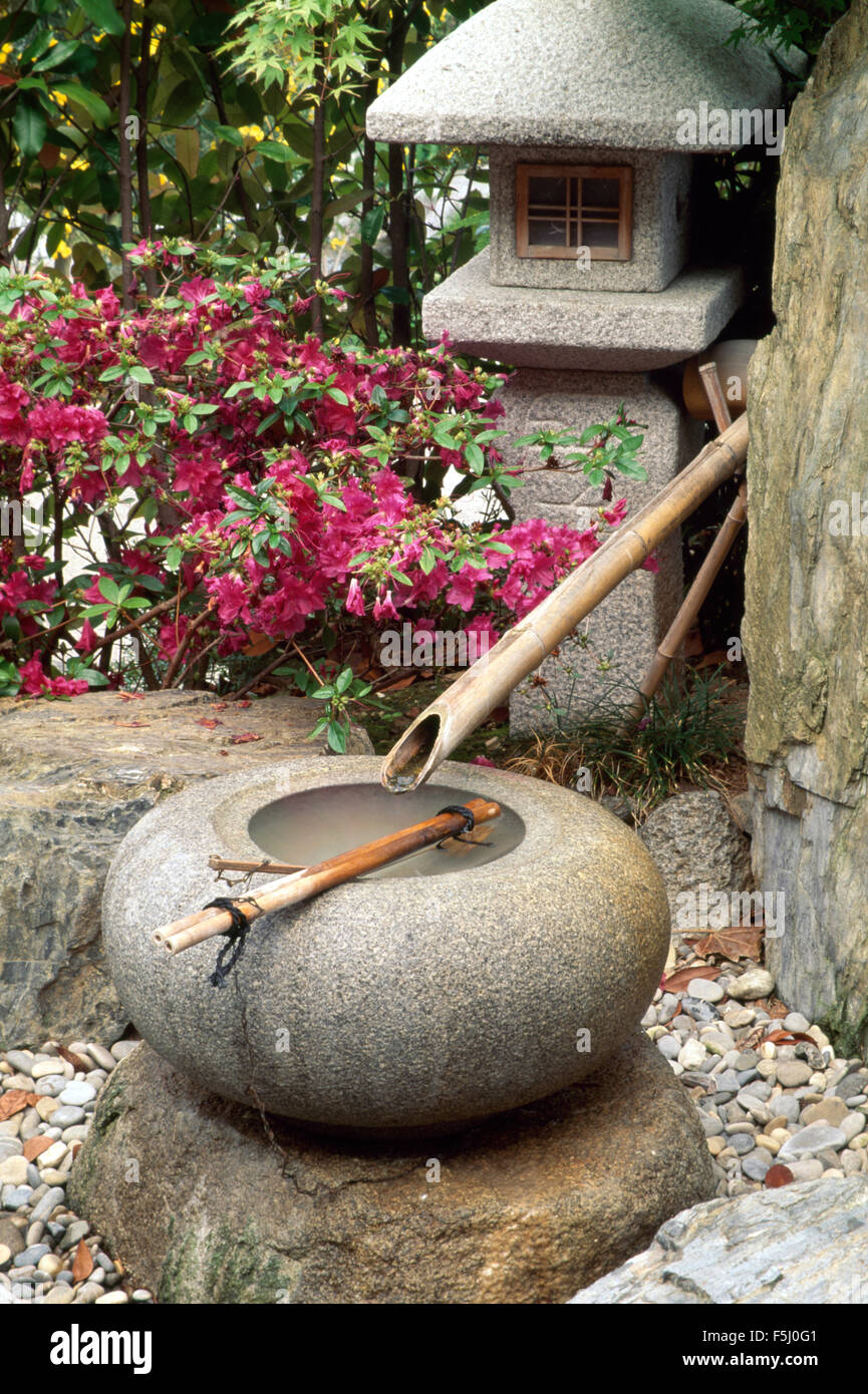 Japanisches Wasserspiel aus Bambus-Rohr und kreisförmige Stein Topf auf der Terrasse mit einer Steinlaterne Stockfoto
