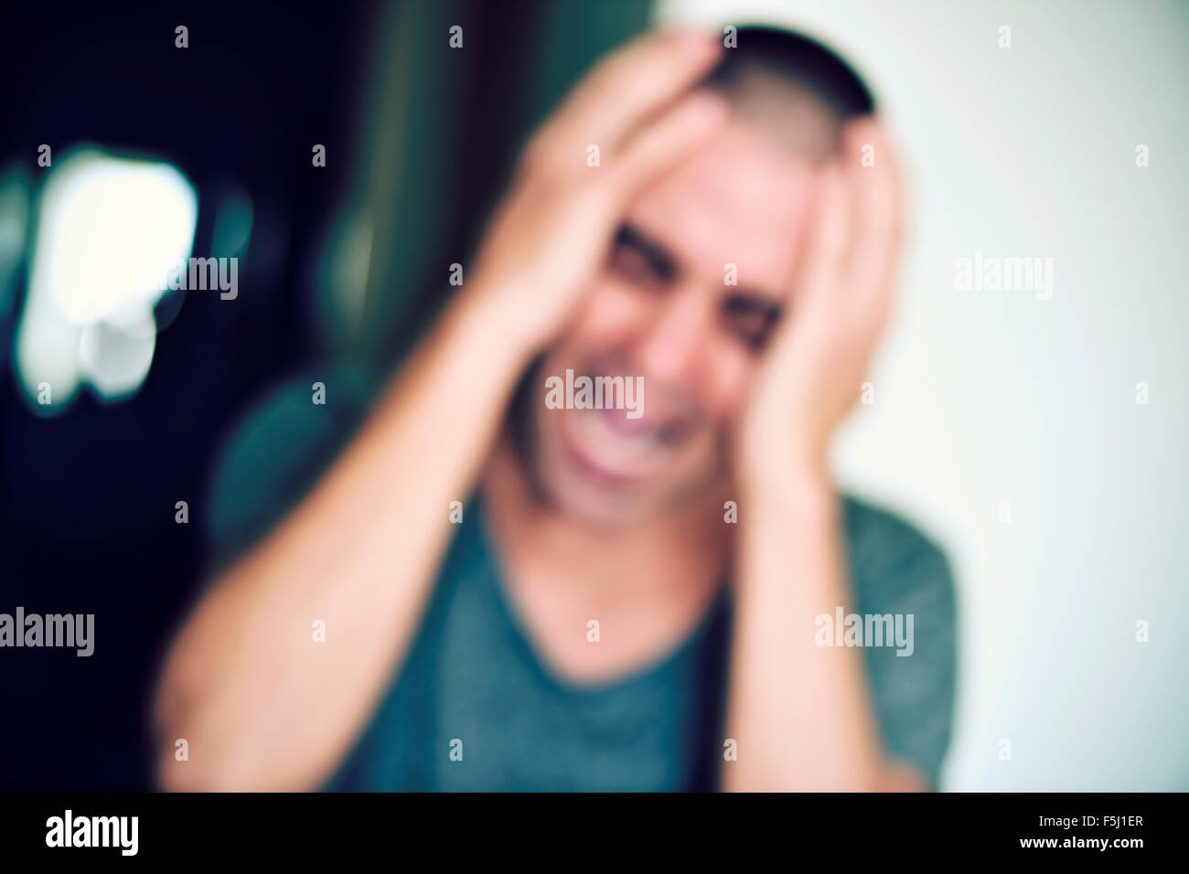 ein unscharfes Bild von einem jungen kaukasischen Mann mit seinen Händen in den Kopf und schreiend im Innenbereich Stockfoto