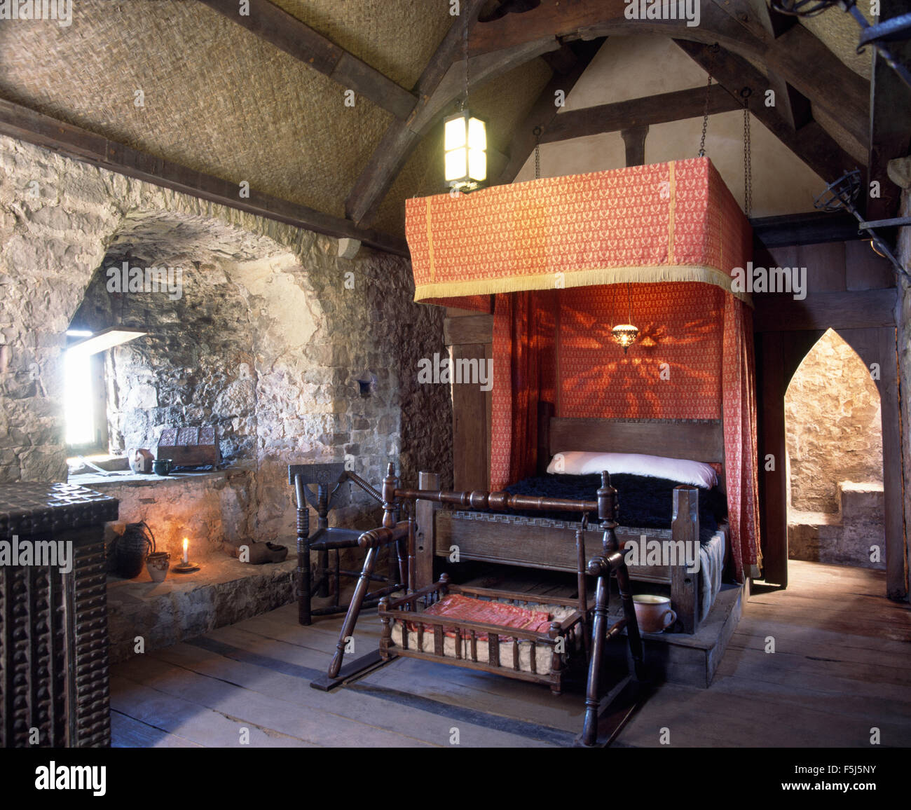 Halbe Tester Bett mit roten Vorhängen und schaukelnden Wiege des Kindes im Schlafgemach auf Penhow Castle in Wales Stockfoto