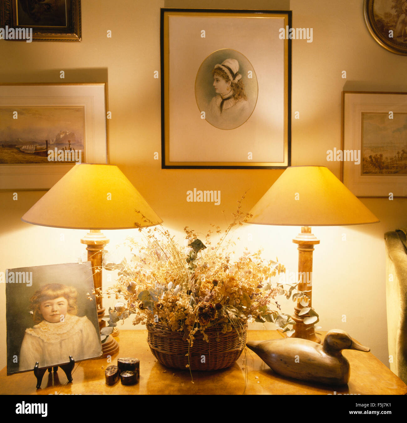 Gruppe von Bildern an der Wand über dem Tisch mit brennenden Lampen und einen Korb mit getrockneten Blumen neben eine Holzente Stockfoto