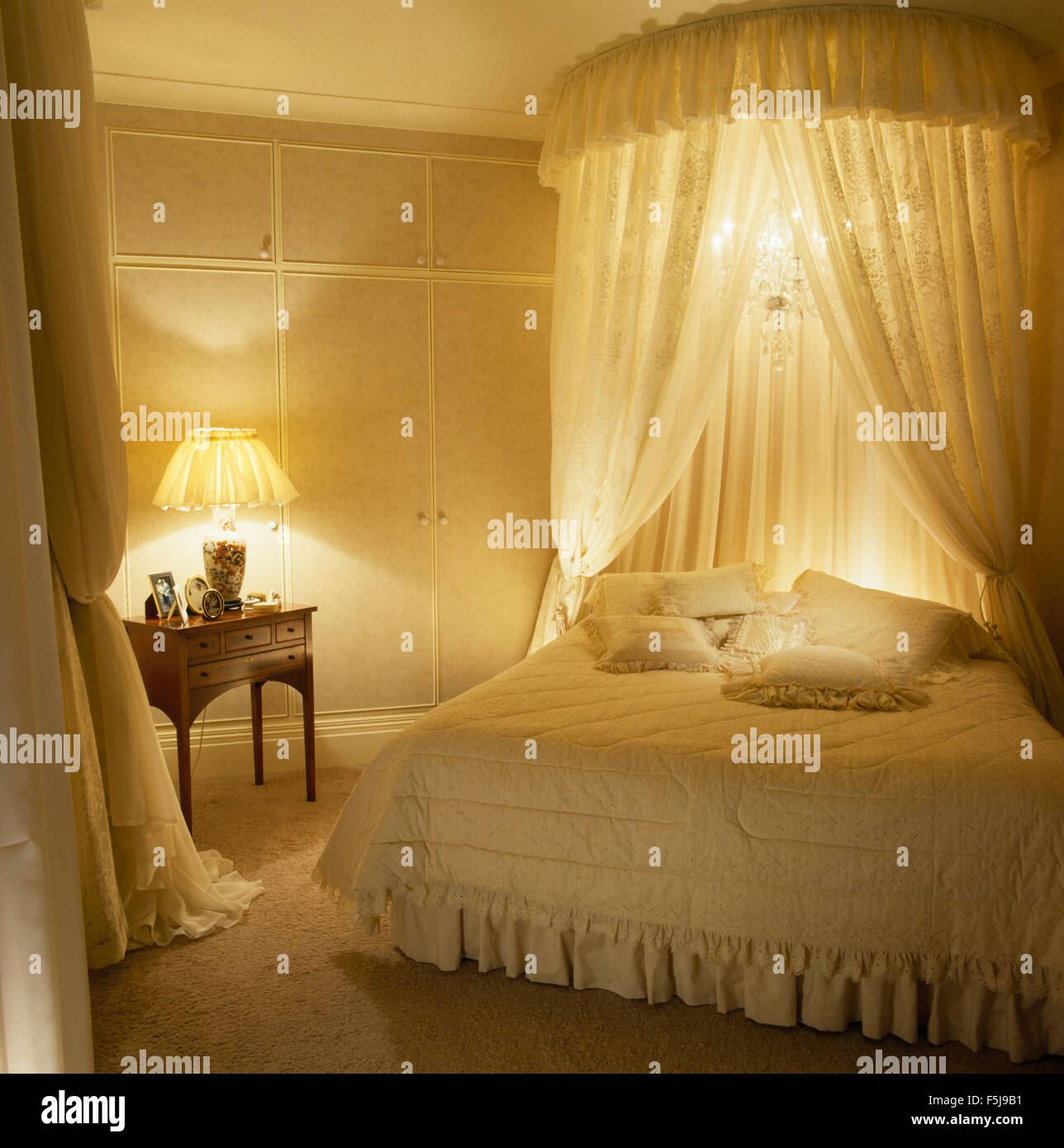 Coronet mit Gardinen und kleiner Kronleuchter über Bett in einem 80er Jahre  Schlafzimmer mit brennenden Lampen Stockfotografie - Alamy