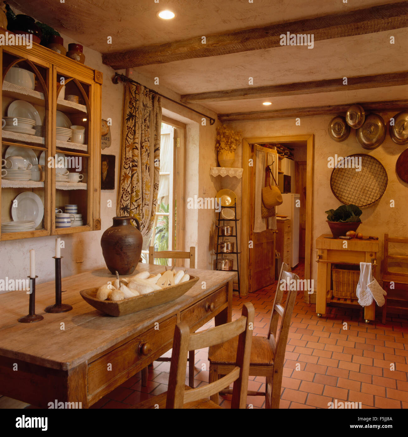 Verglasten Schrank an Wand über eine alte Kiefer Esstisch und Stühle in einer Landhausküche mit einem Ziegelstein gefliesten Boden Stockfoto