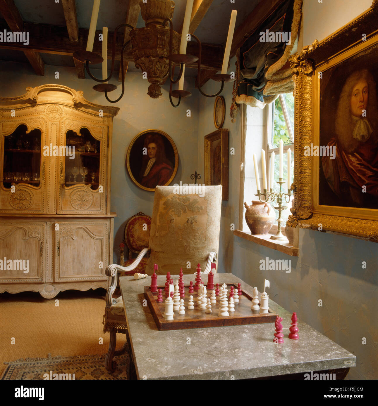 Kerzen in Metall Kronleuchter oben Marmortisch mit einem Schachspiel in einem Land-Wohnzimmer mit einem antiken Schrank Stockfoto
