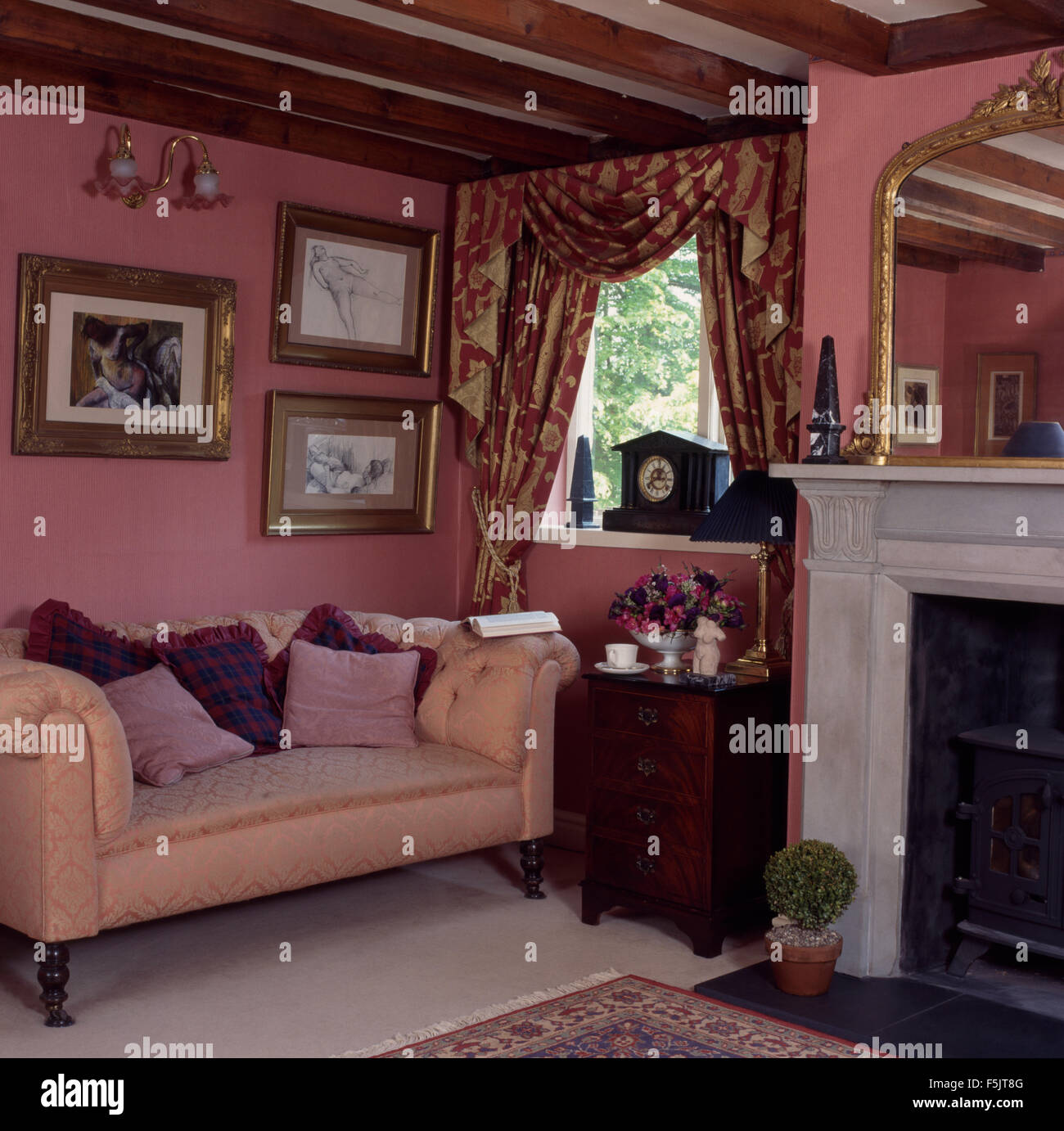 Chesterfield-Sofa in dunkelrosa der neunziger Jahre ein Ferienhaus Wohnzimmer mit swagged + tailed Vorhänge und eine kleine antike Kommode Stockfoto