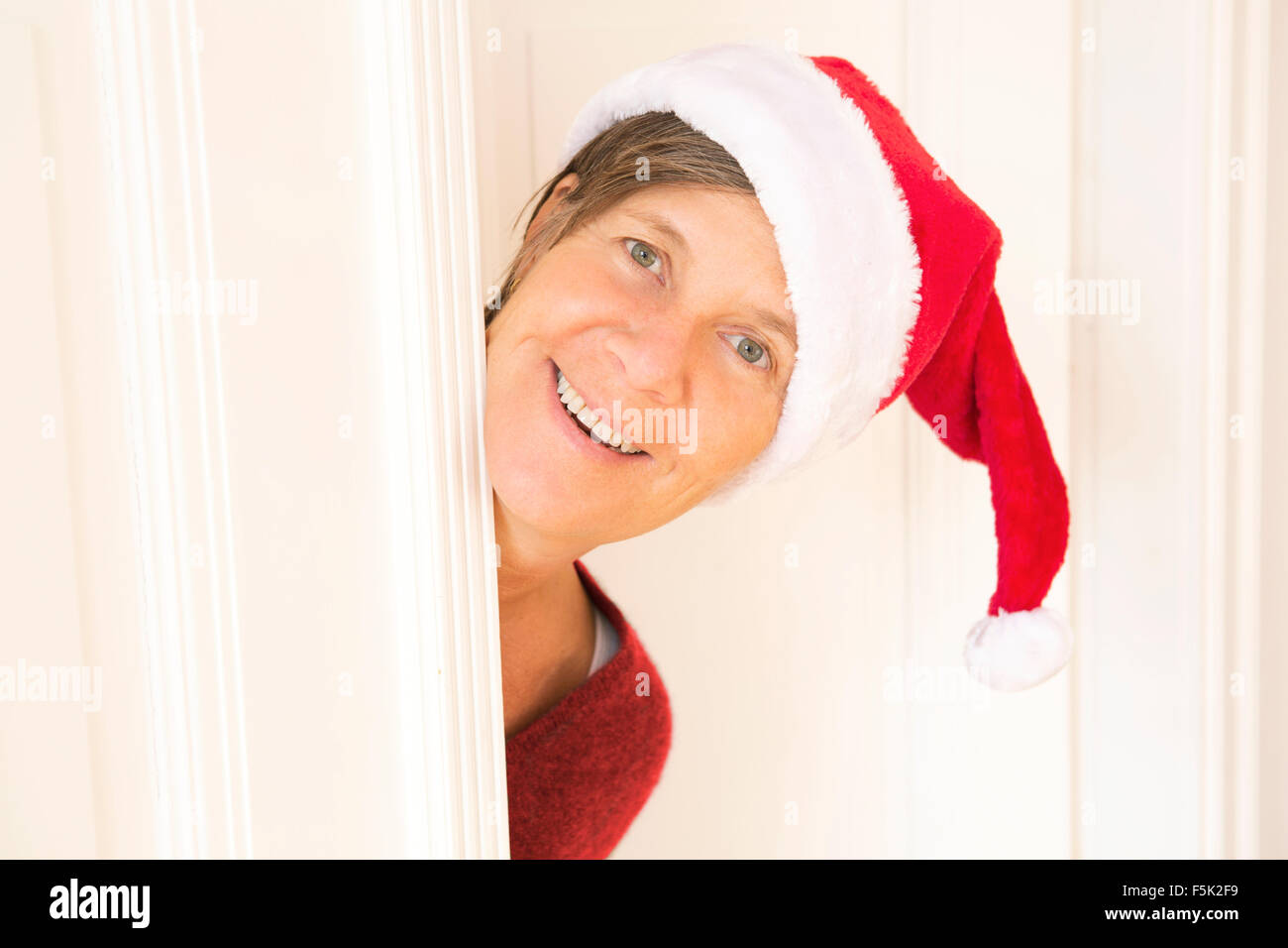 Frau mit Nikolausmütze Blick hinter einer Tür und lächelt Stockfoto