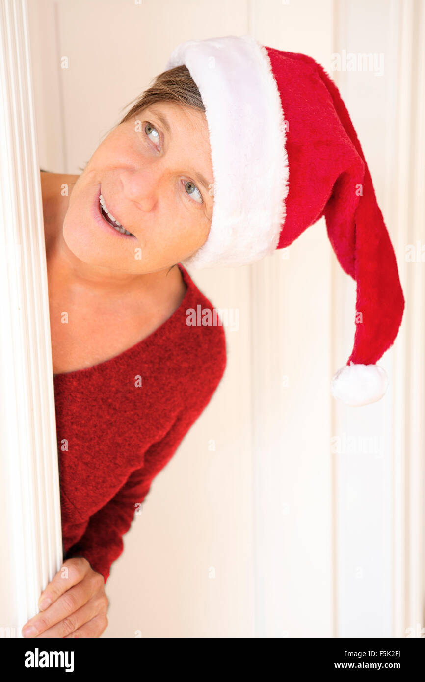 Frau mit Nikolausmütze Blick hinter einer Tür und lächelt Stockfoto