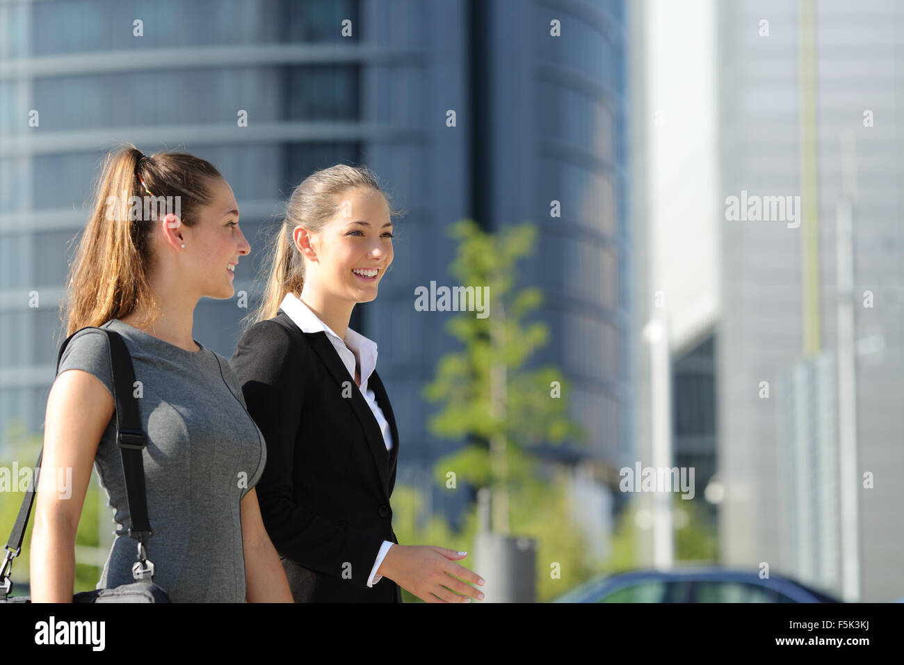 Zwei glückliche Geschäftsfrauen gehen und sprechen auf der Straße mit Bürogebäude im Hintergrund Stockfoto