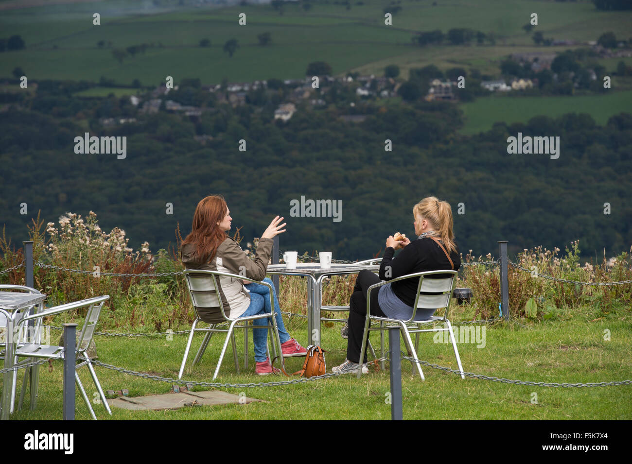 2 Freundinnen sitzen draußen, essen und plaudern im Cow & Calf Rock Café, Ilkley, Yorkshire, UK - landschaftlich schöner Ort mit Panoramablick über das Tal. Stockfoto