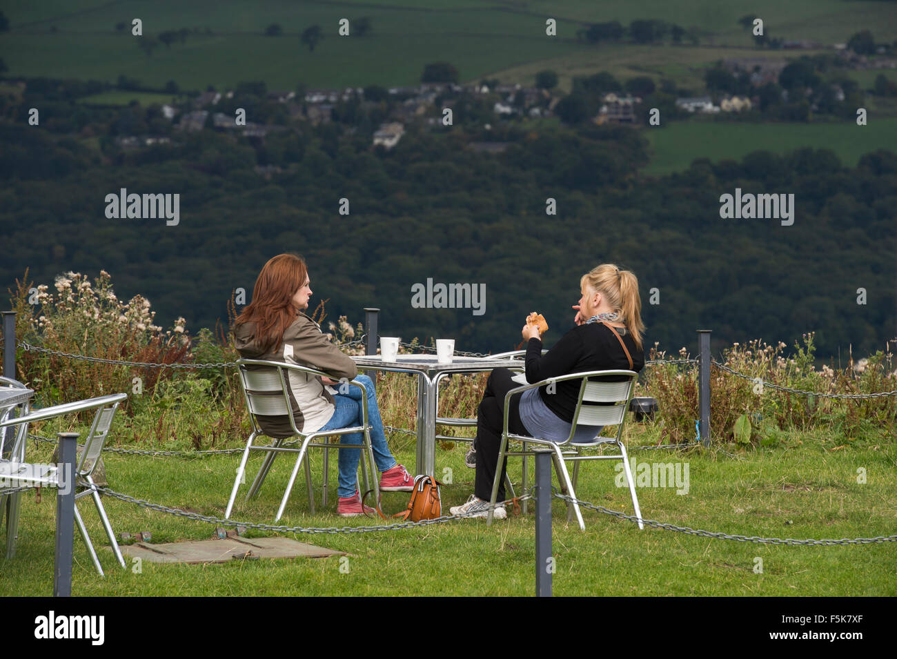 2 Freundinnen sitzen draußen, essen und plaudern im Cow & Calf Rock Café, Ilkley, Yorkshire, UK - landschaftlich schöner Ort mit Panoramablick über das Tal. Stockfoto