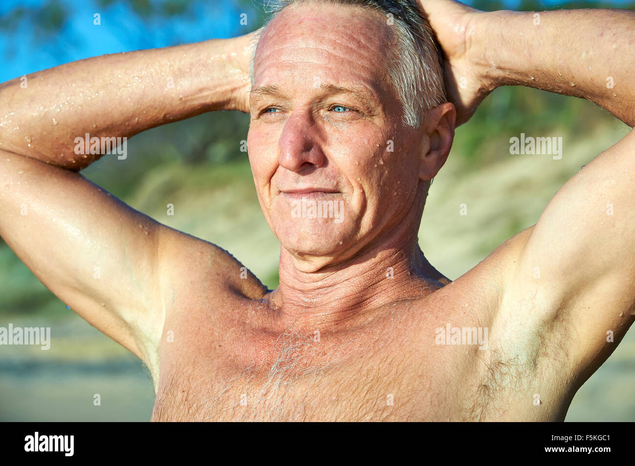 Kopf und Schulter Porträt von einem reifen Alter Mann lächelnd mit Sanddünen und Baum im Hintergrund Stockfoto