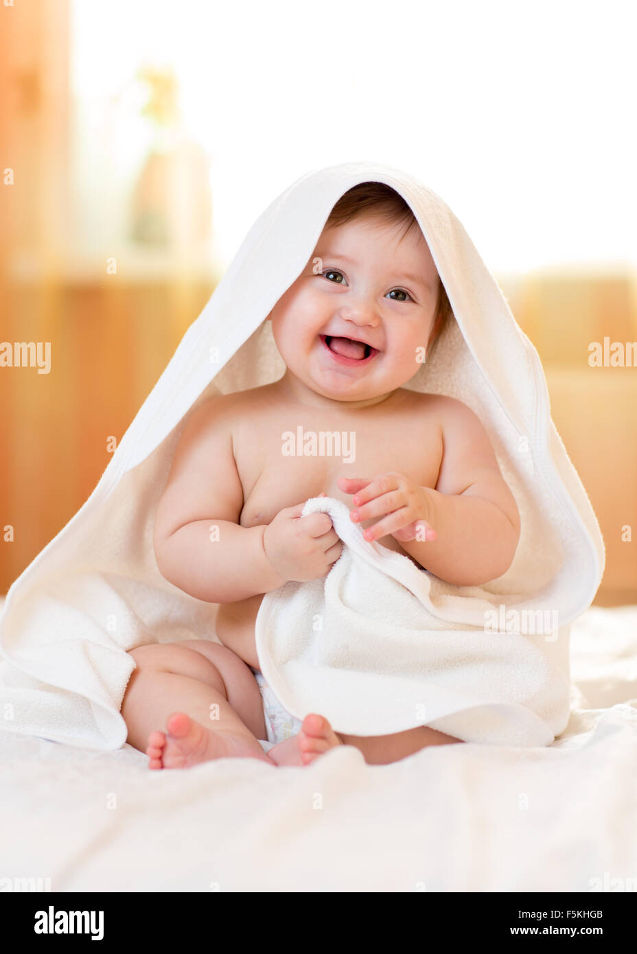 Lächelndes Babymädchen unter weißen Handtuch nach dem Baden Stockfoto