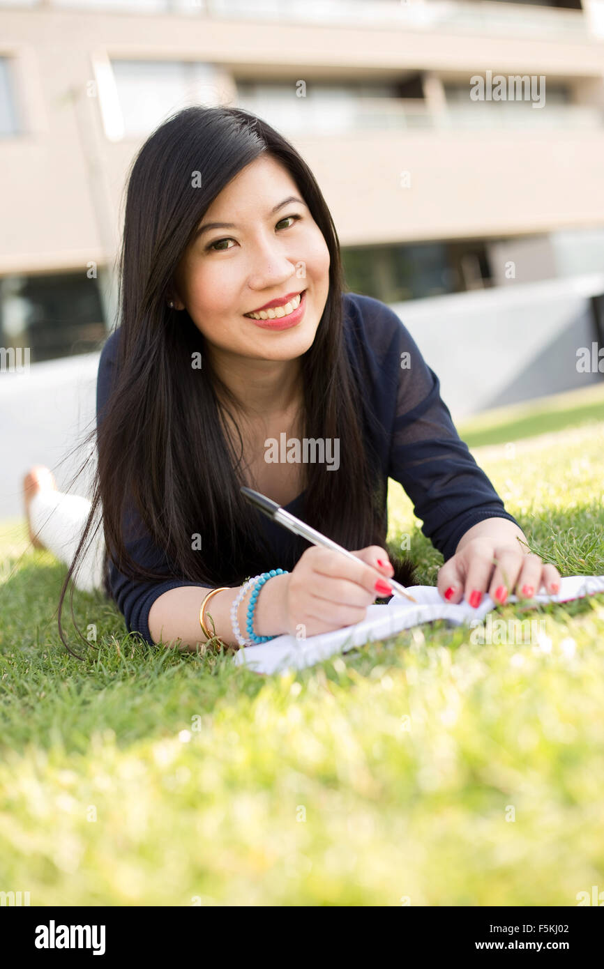 Japanischer Student liegend auf dem Rasen mit einem Lehrbuch Stockfoto