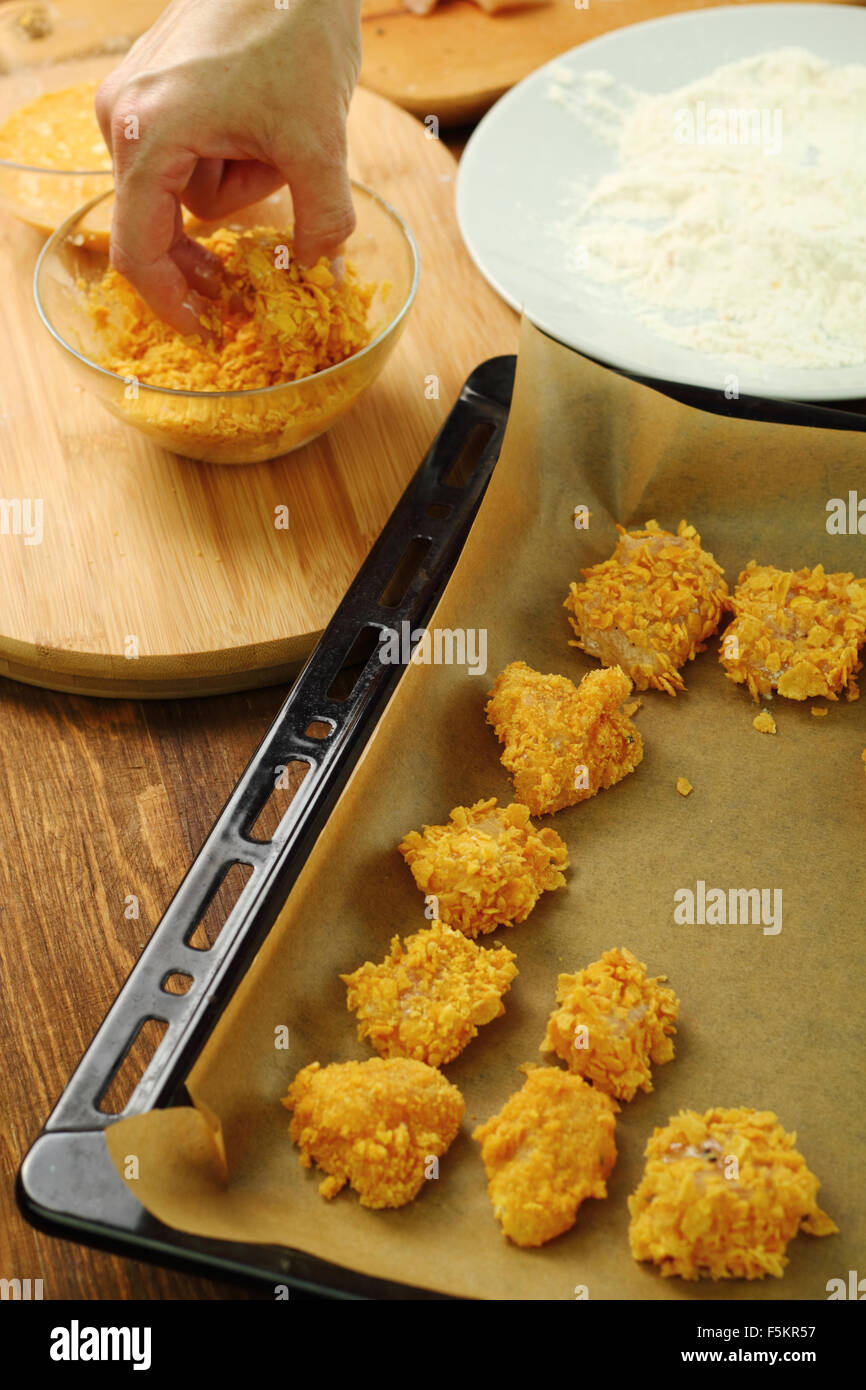Rollen Sie bemehlten, angestachelt Hähnchenfilet in Mais Flocken Krümel. Ofen gebacken Mais Flocken Krümel Hähnchen-Nuggets. Serie. Stockfoto