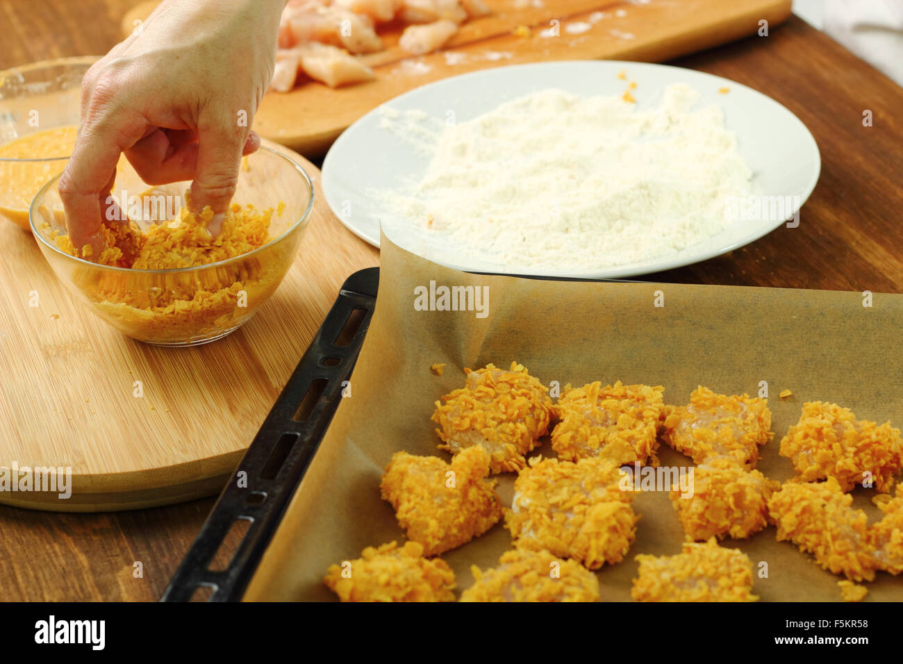 Rollen Sie bemehlten, angestachelt Hähnchenfilet in Mais Flocken Krümel. Ofen gebacken Mais Flocken Krümel Hähnchen-Nuggets. Serie. Stockfoto