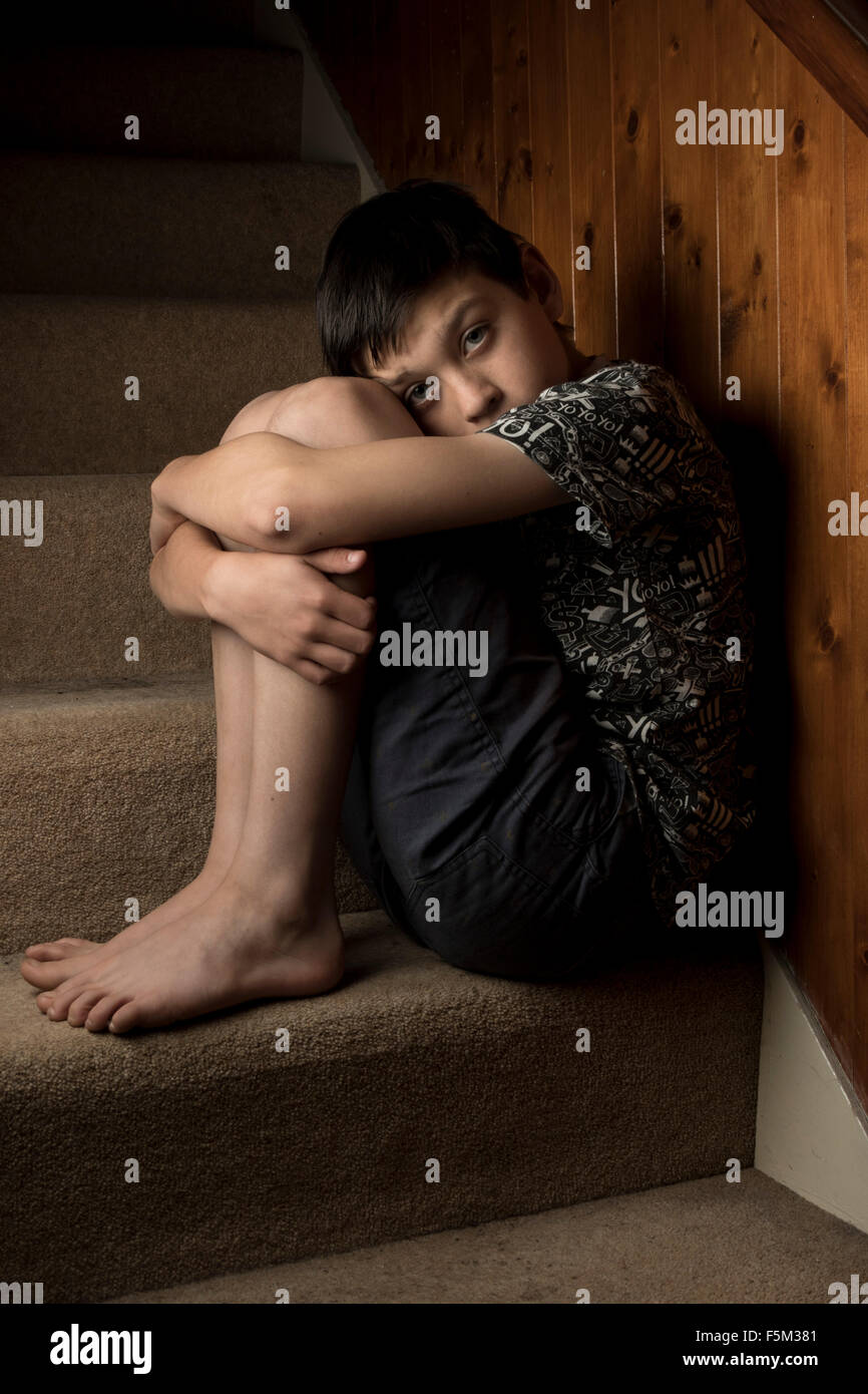 Traurig, schikaniert oder missbrauchte Junge sitzt auf der Treppe Stockfoto