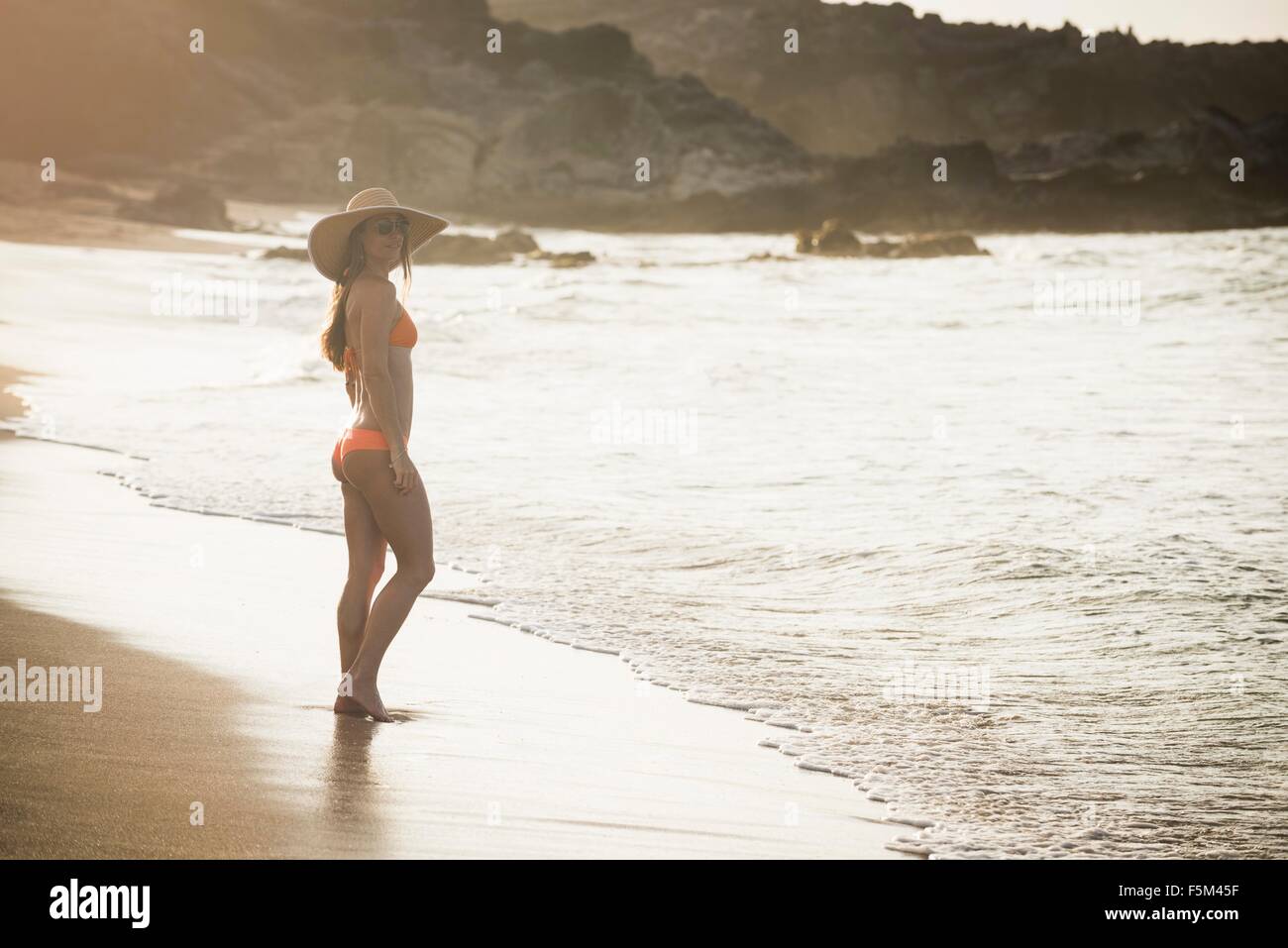 Mitte Erwachsene Frau tragen Sonnenhut und Bikini stehen am Strand, Maui, Hawaii, USA Stockfoto