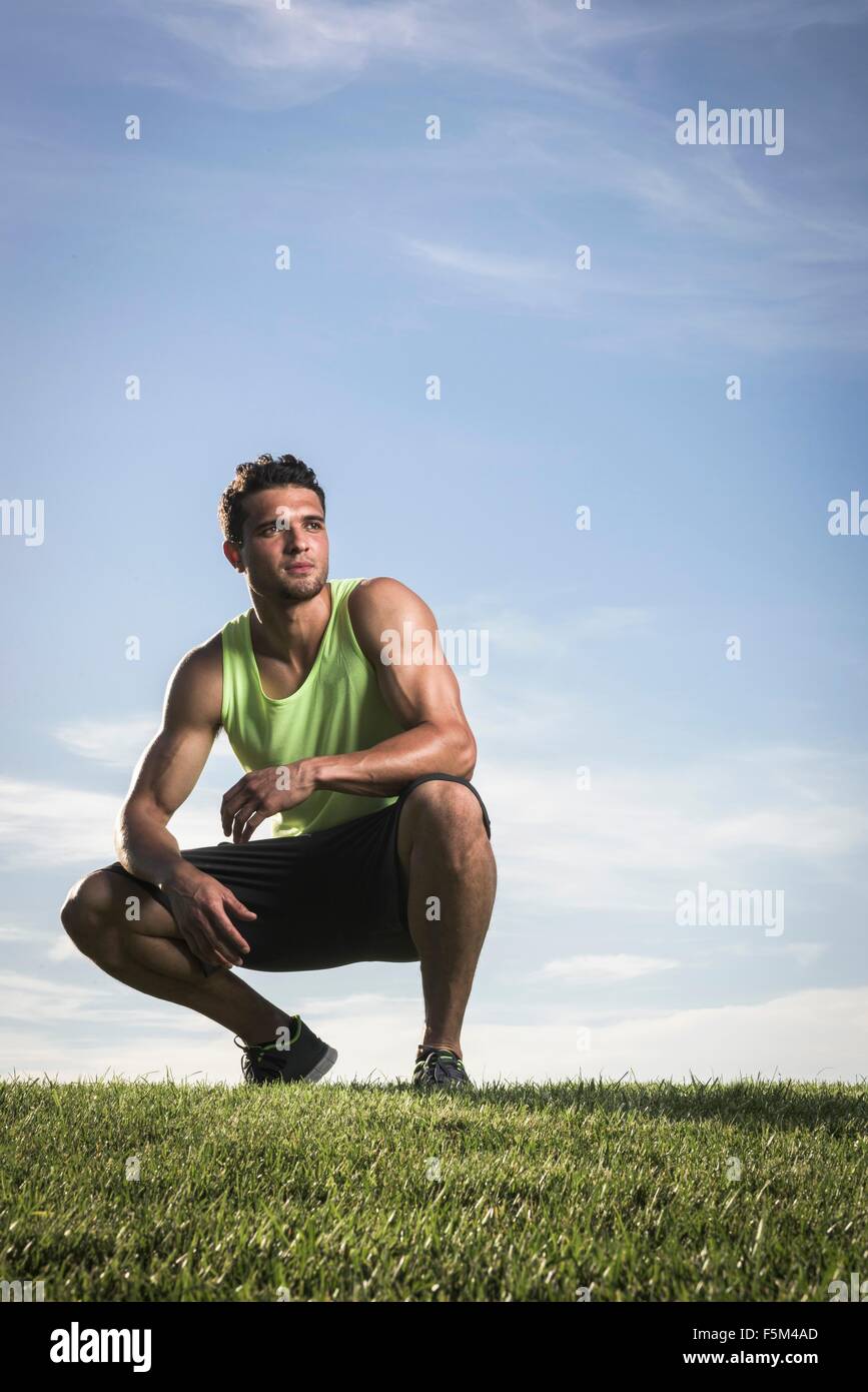 Porträt von zuversichtlich athletischen jungen Mann kauert im park Stockfoto
