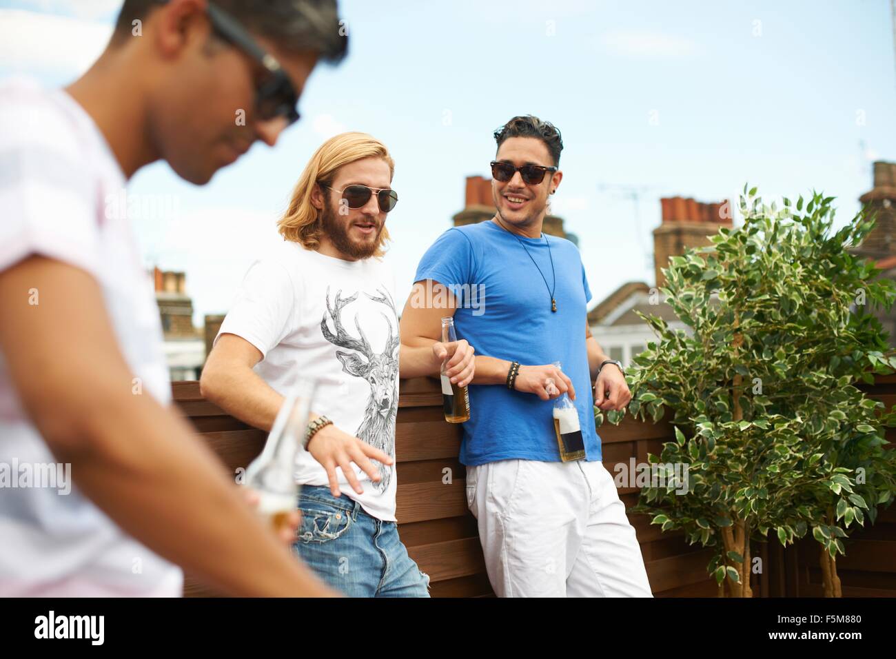 Drei männliche Freunde trinken Bier am Grill auf dem Dach Stockfoto
