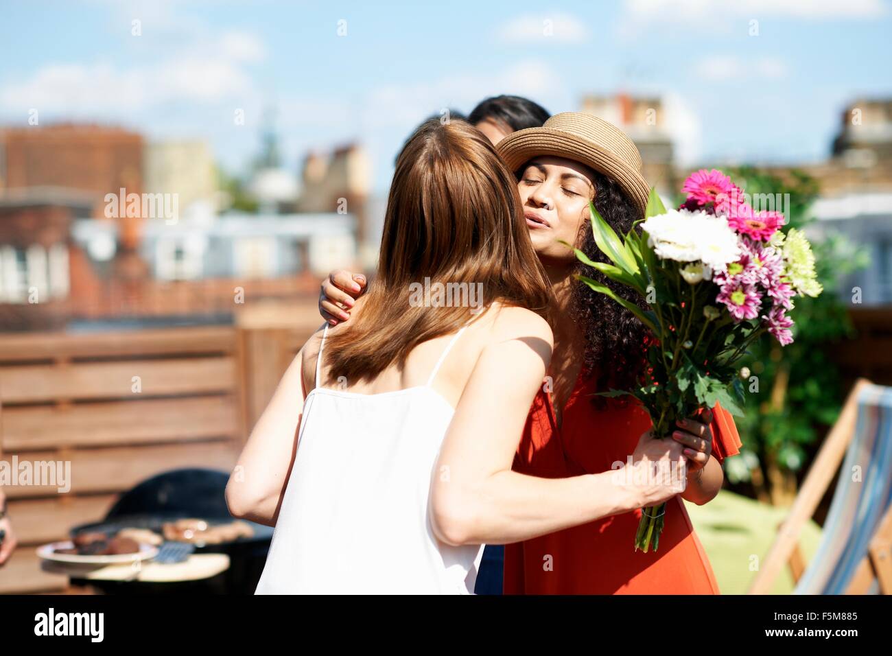 Freundinnen Gruß mit Blumenstrauß an Dachterrasse Grill Stockfoto