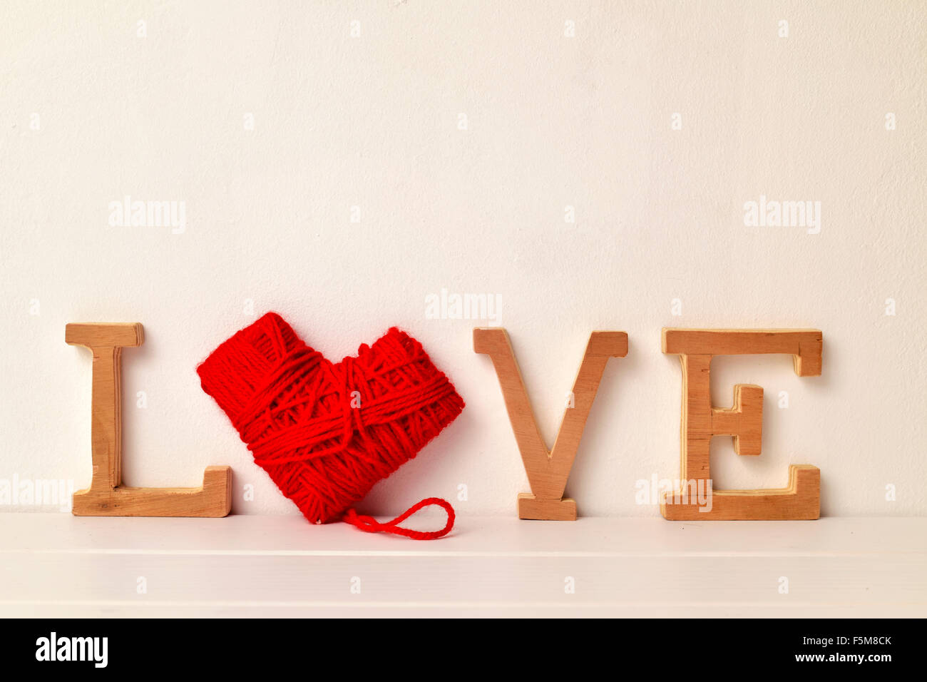 einige Holzbuchstaben und einer herzförmigen Spule des roten Garn bilden das Wort Liebe Stockfoto