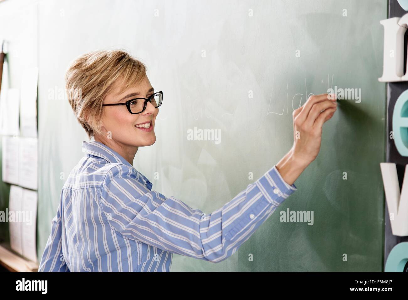 Lehrerin im Klassenzimmer, auf Tafel schreiben Stockfoto