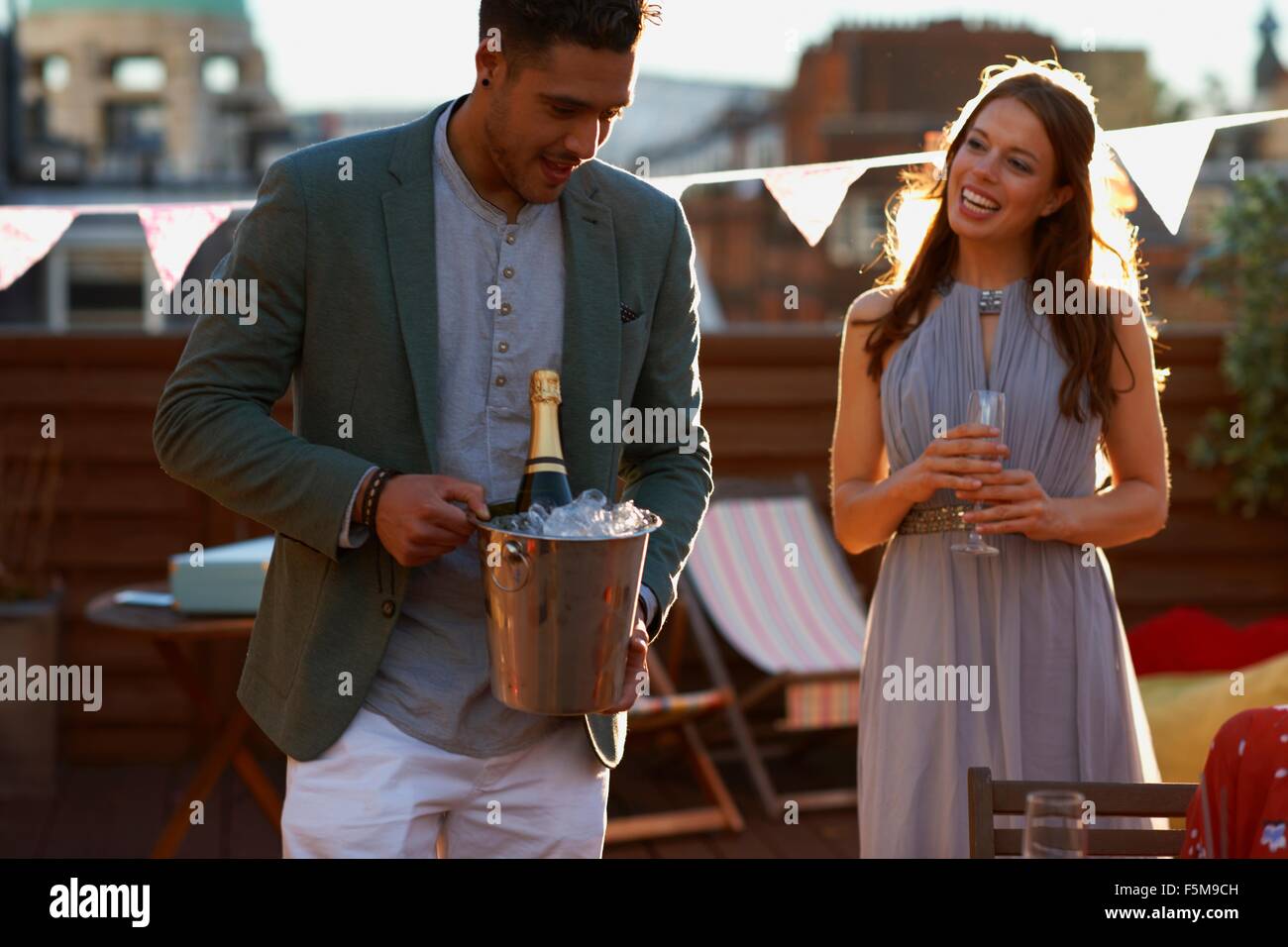 Mitte erwachsenes paar auf Party auf Dachterrasse halten Eiseimer mit Champagner lächelnd Stockfoto