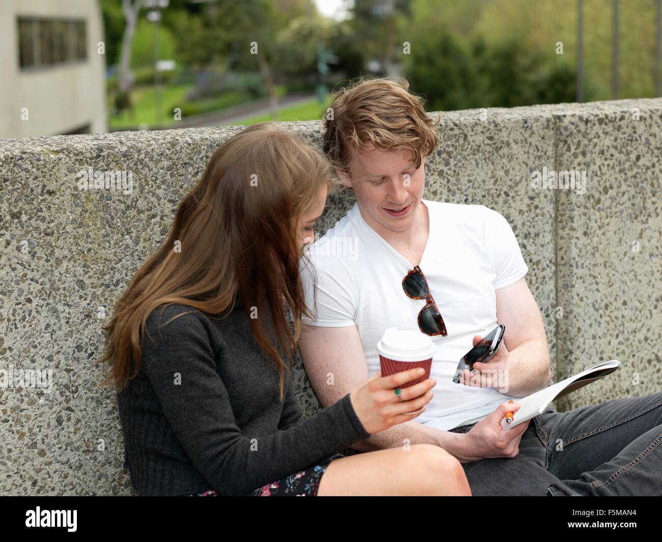 Junges Paar Kaffeetrinken, mit Smartphone gegen Betonwand, Melbourne, Victoria, Australien Stockfoto