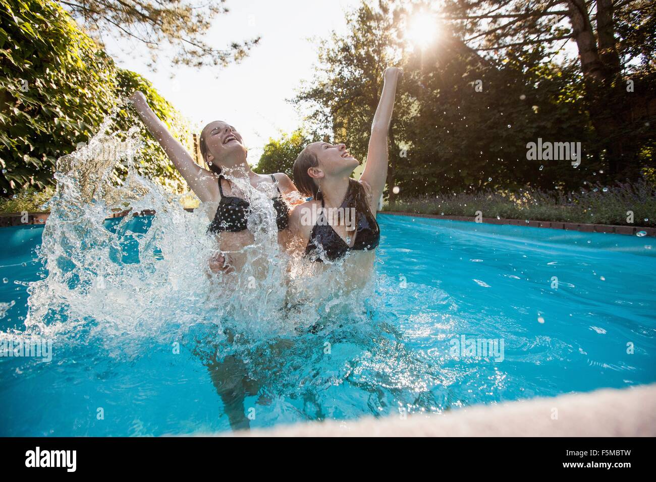 Zwei Mädchen im Teenageralter mit Schwimmbad erhobenen Armen springen Stockfoto