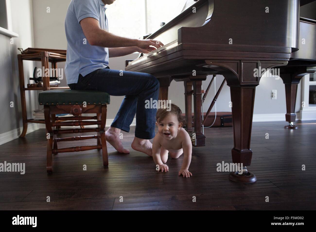 Vater mit Baby zu Füßen kriechen Klavier spielen Stockfotografie - Alamy