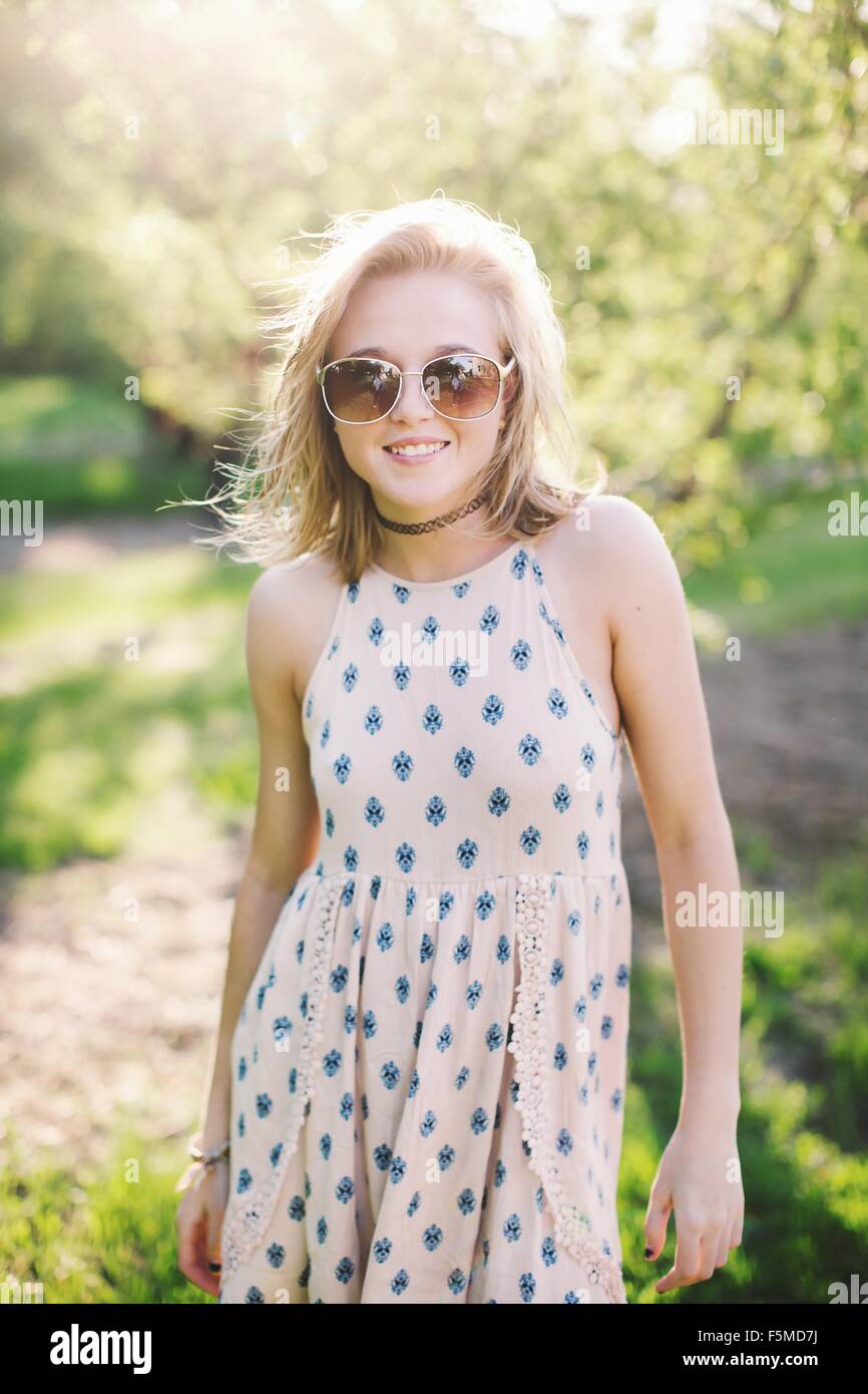 Junge Frau trägt ärmelloses Kleid und Sonnenbrille Kamera Lächeln betrachten Stockfoto