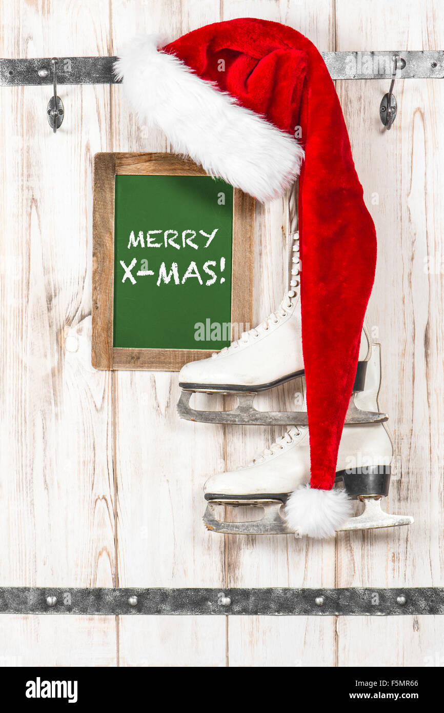 Roter Hut für Santa Claus und weiße Schlittschuhe. Vintage-Stil-Weihnachts-Dekoration mit Tafel mit Beispieltext Frohe Weihnachten! Stockfoto