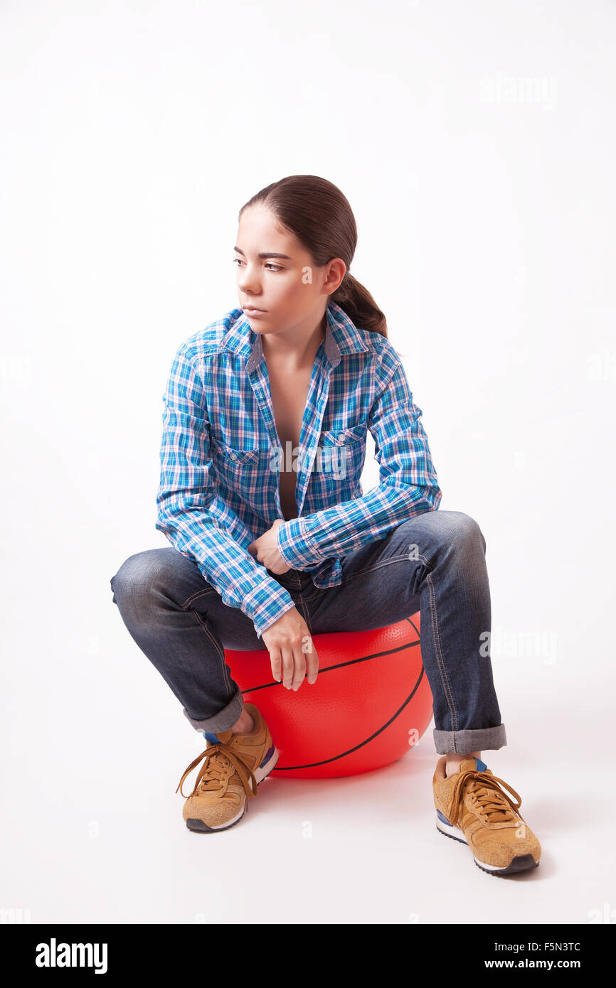 Attraktive junge Frau in einem blauen Hemd und Jeans sitzt am ball Stockfoto