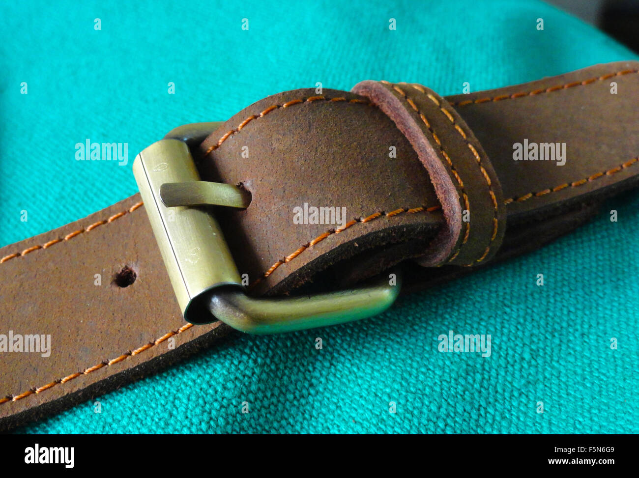 Brauner Ledergürtel mit Messing-Schnalle auf grün Baumwolltuch Stockfoto
