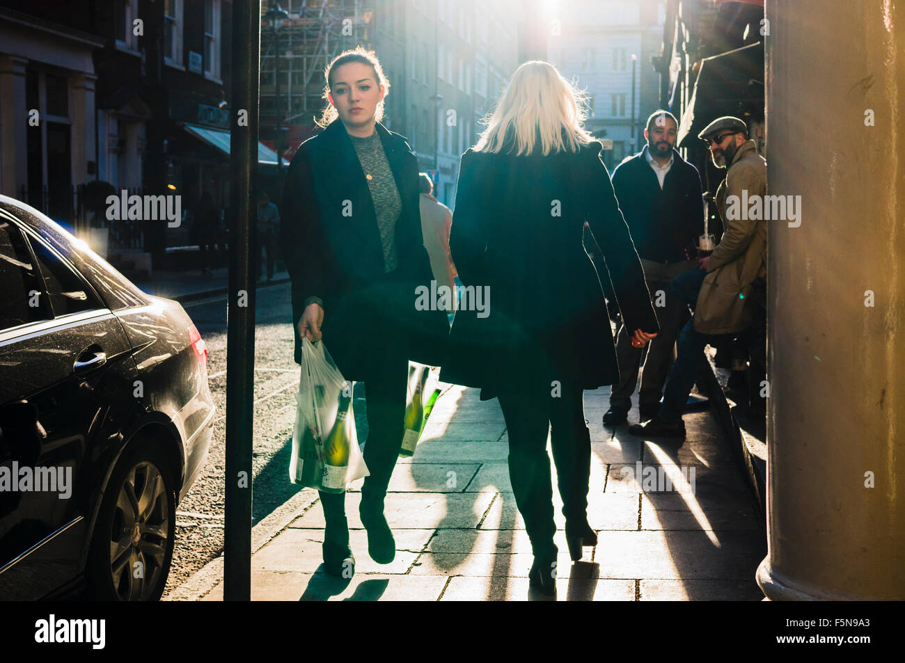Zwei Männer beobachten zwei Frauen zu Fuß vorbei an einer Bar in Soho, London an einem sonnigen Nachmittag. Stockfoto