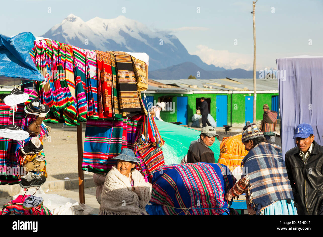 Eine indigene Frau Verkauf von traditionellen bunten bolivianischen Stoff auf einem Straßenmarkt in El Alto, La Paz, Bolivien, Südamerika, mit der Spitze des Illimani im Hintergrund. Stockfoto