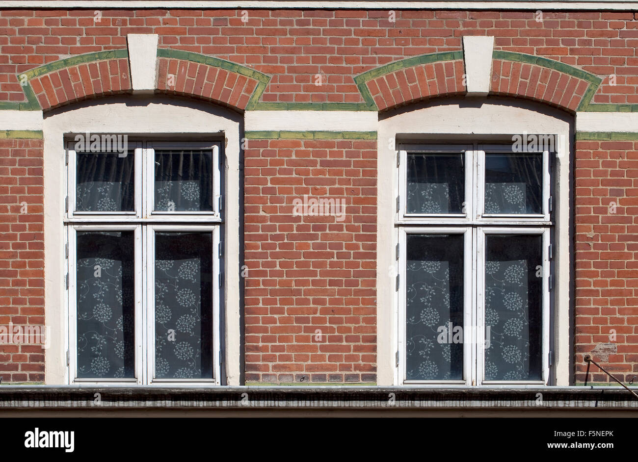 Grün glasierte Ziegel Gliederung und einfache Gardinen machen diese zwei Fenster schauen, einladend und interessant. Stockfoto