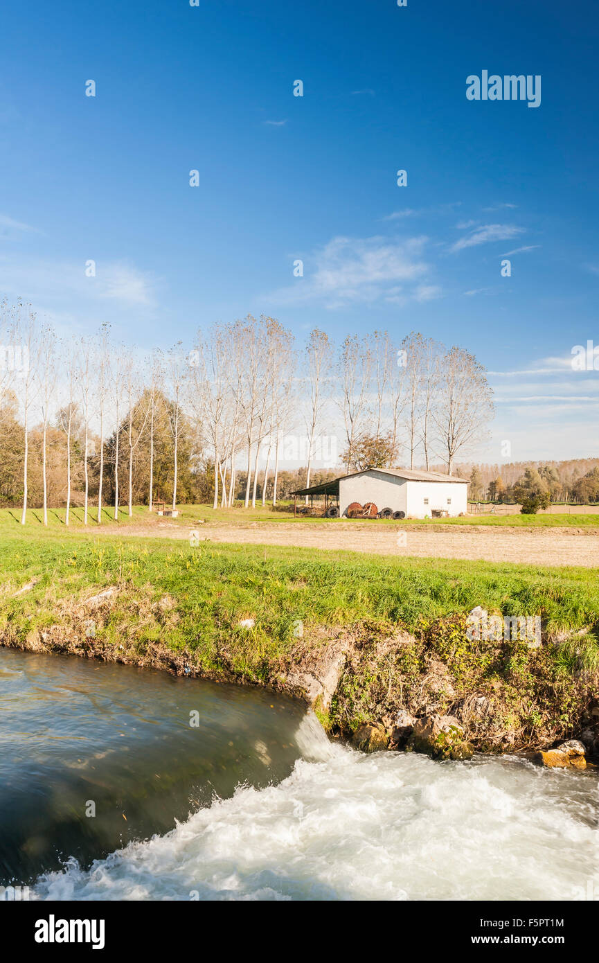 Agrarlandschaft mit einem Fluss, Wasserfall, Pappeln und ein altes Werkzeug zu vergießen. Stockfoto