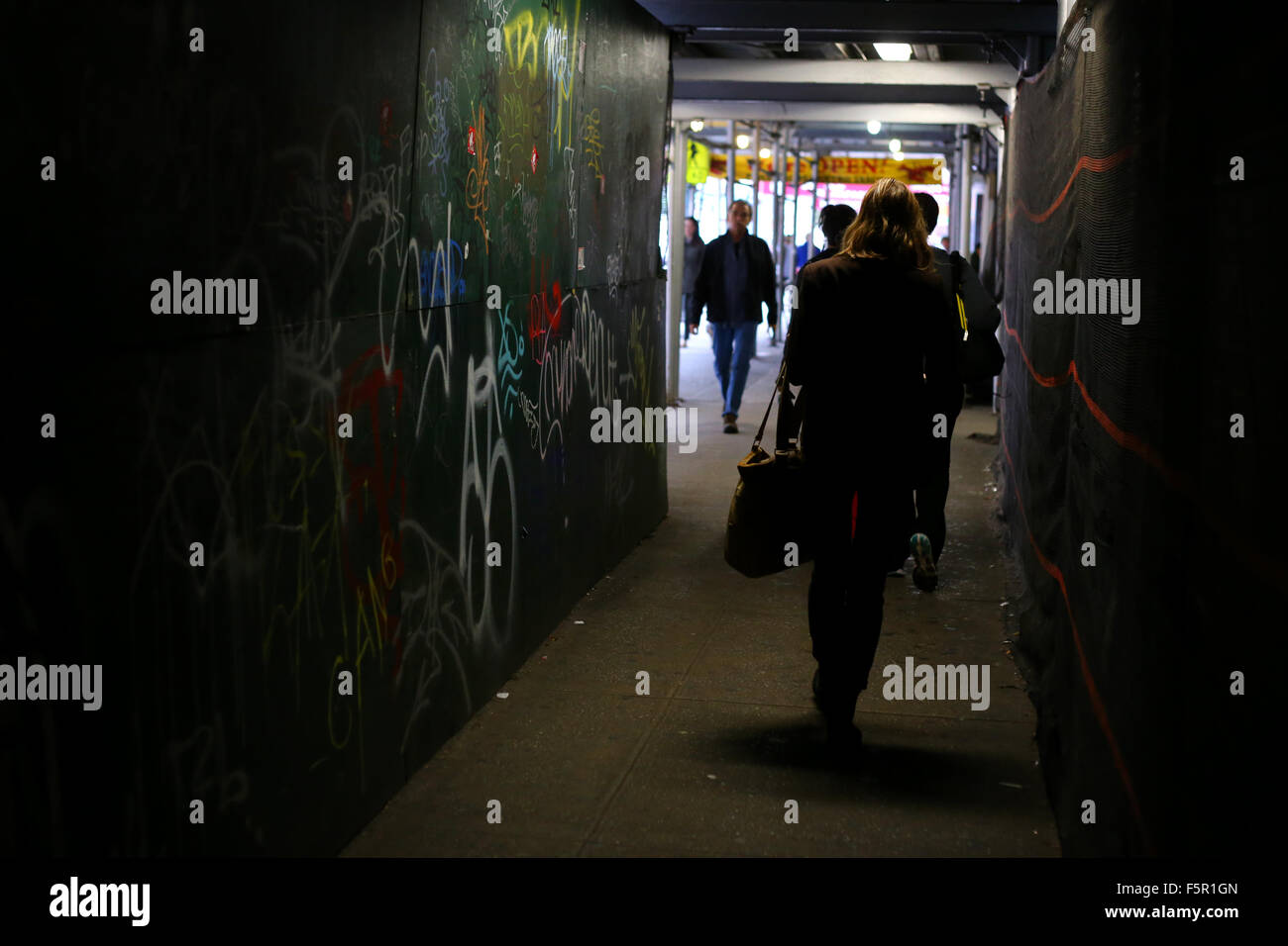 Menschen und Pendler gehen durch ein schwach beleuchtetes Gehsteig-Gerüst, das einen schmalen Durchgang auf einer Baustelle in New York City bildet Stockfoto