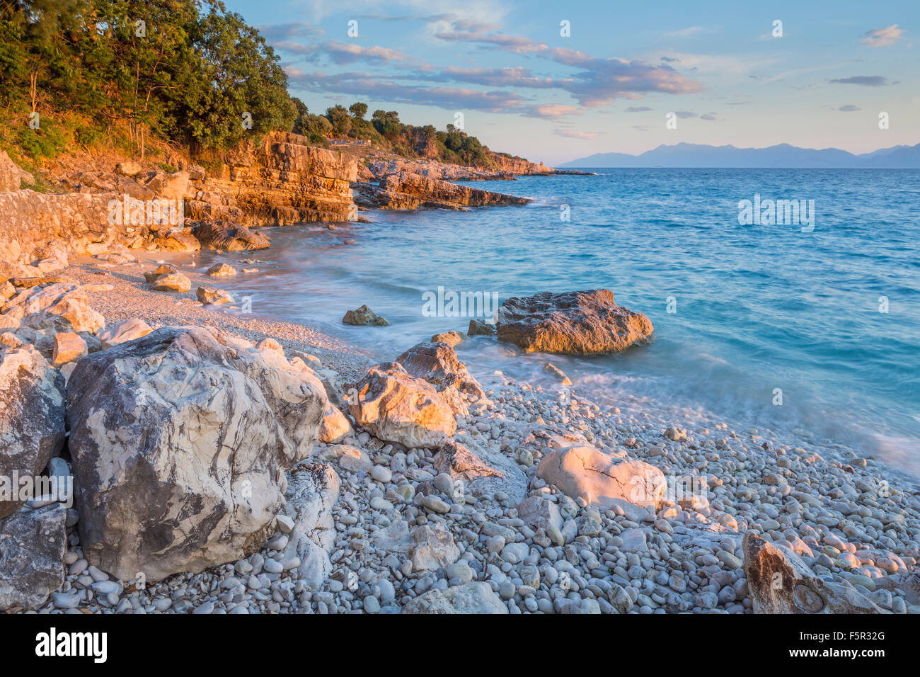 Die Kieselsteine und Felsen auf Bataria Strand, Kassiopi, Korfu Leuchten mit dem Stong orange Licht des Sonnenaufgangs. Stockfoto