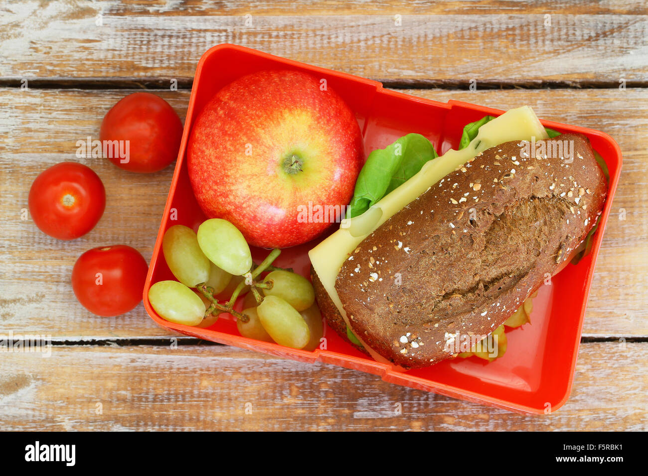 Gesunde Schule-Lunch-Box mit Vollkorn Brötchen mit Käse und Salat, Kirschtomaten, roten Apfel und Trauben Stockfoto