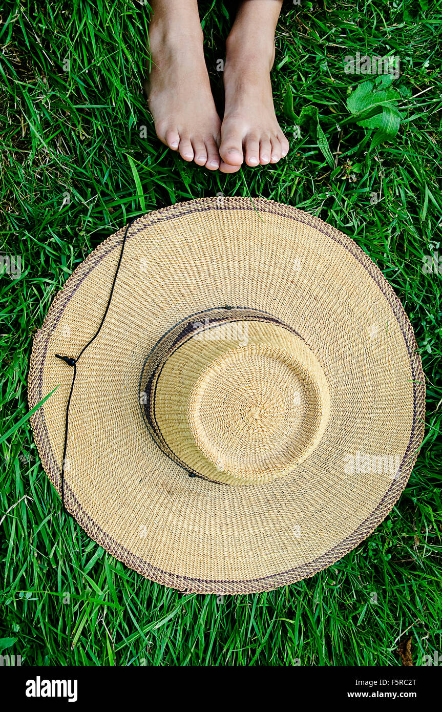 Einen großen Strohhut Verlegung auf dem Rasen mit Füßen ragt. Stockfoto