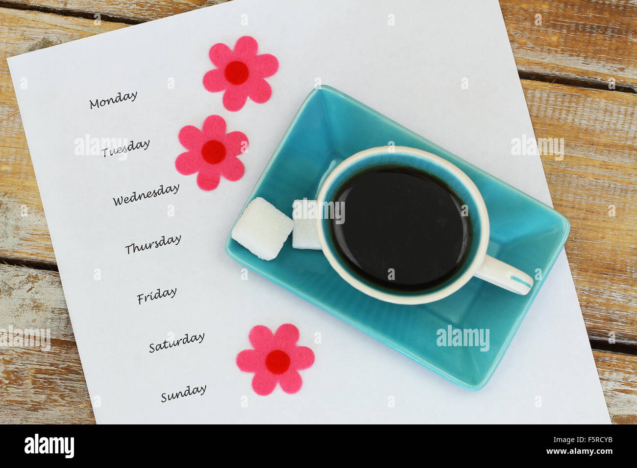 Tasse Kaffee und Wochentagen geschrieben auf weißem Papier und bunte Blumen Stockfoto