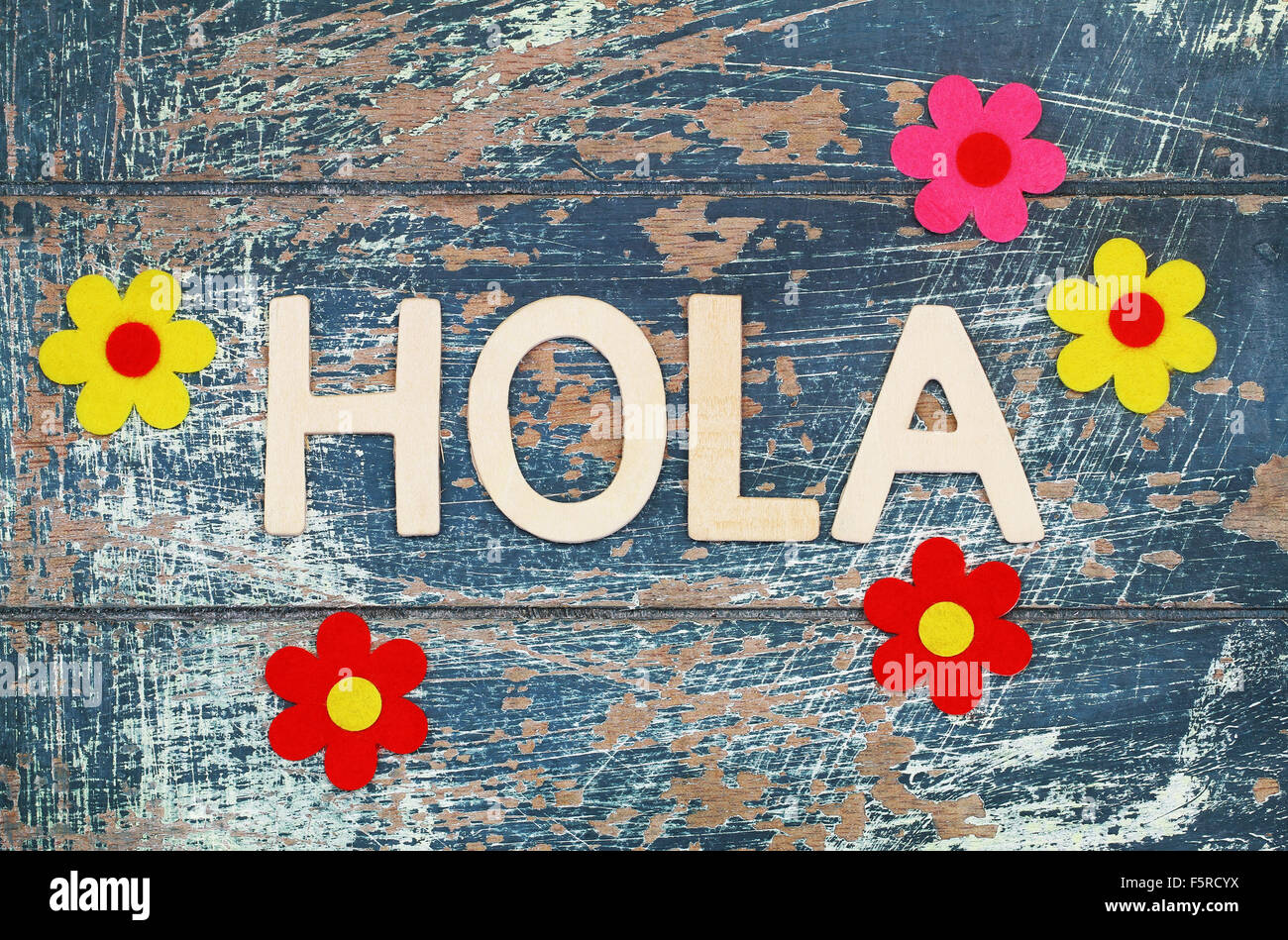 Hola (d.h. Hallo auf Spanisch) mit Holzbuchstaben auf rustikale Oberfläche und bunte Blumen geschrieben Stockfoto