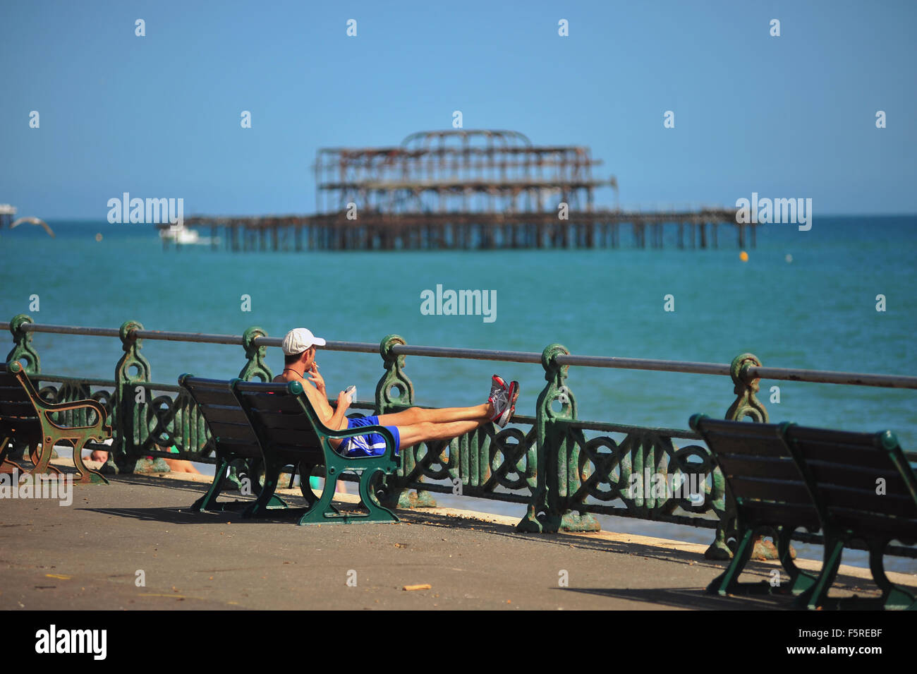 Ein Mann sitzt auf einer Bank an der Brighton Strandpromenade sonniges Juli-Wetter zu genießen. Stockfoto