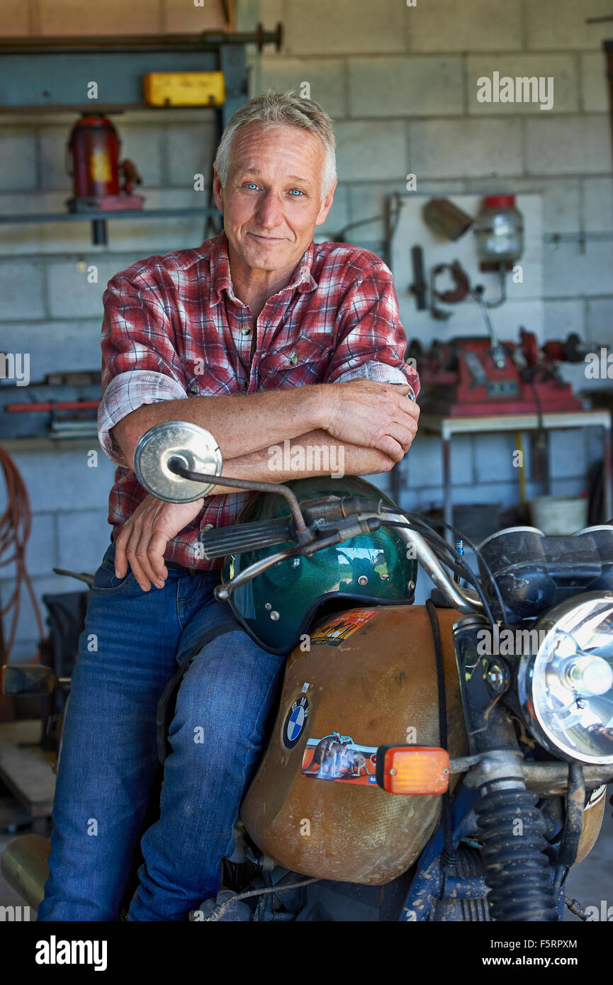 Reifer Alter Mann sitzt auf seinem Motorrad in seiner Scheune/Werkstatt Stockfoto