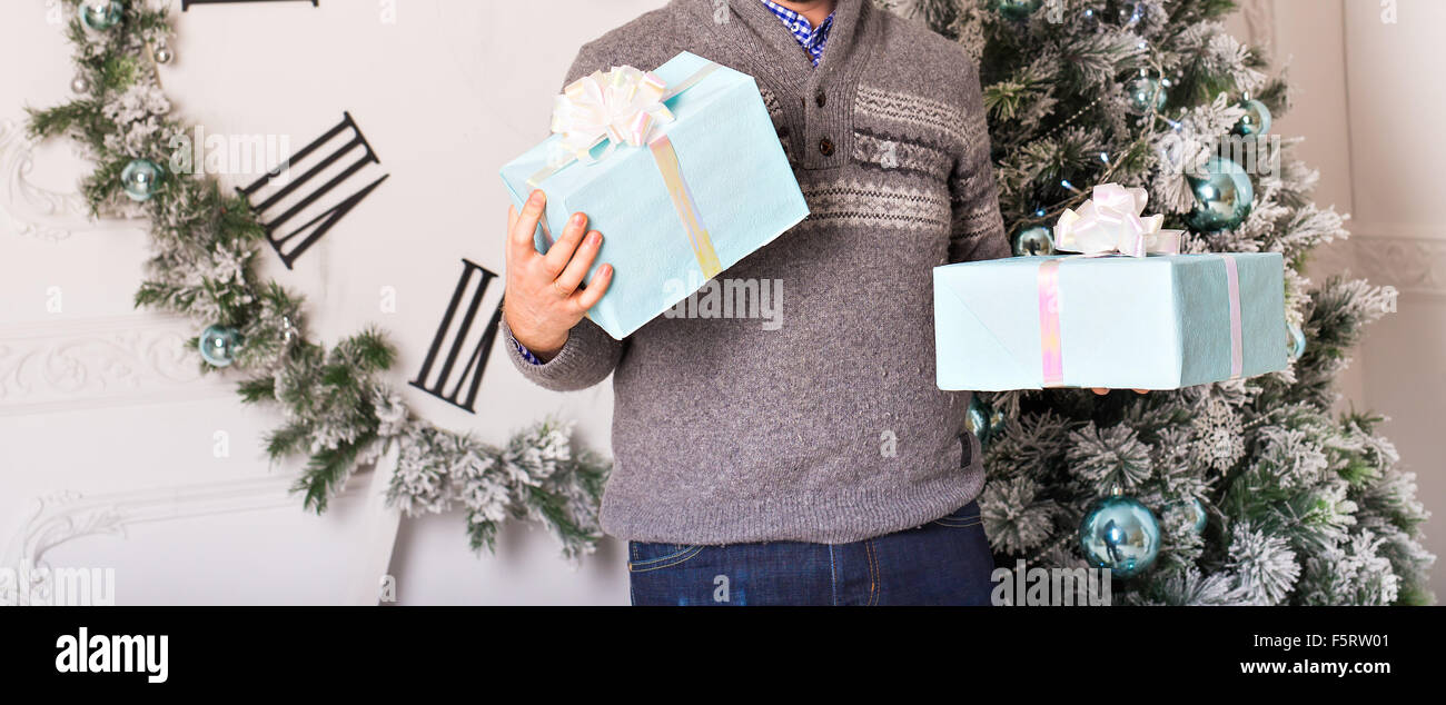 Junger Mann hält Geschenke vor Weihnachtsbaum Stockfoto