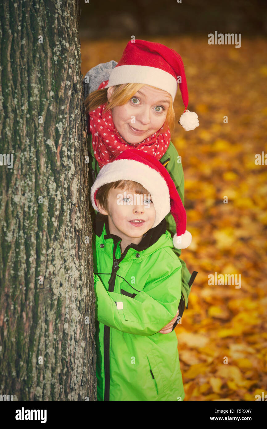 Mutter und Sohn mit Santa Hüte suchen um einen Baum im Park im Herbst Stockfoto